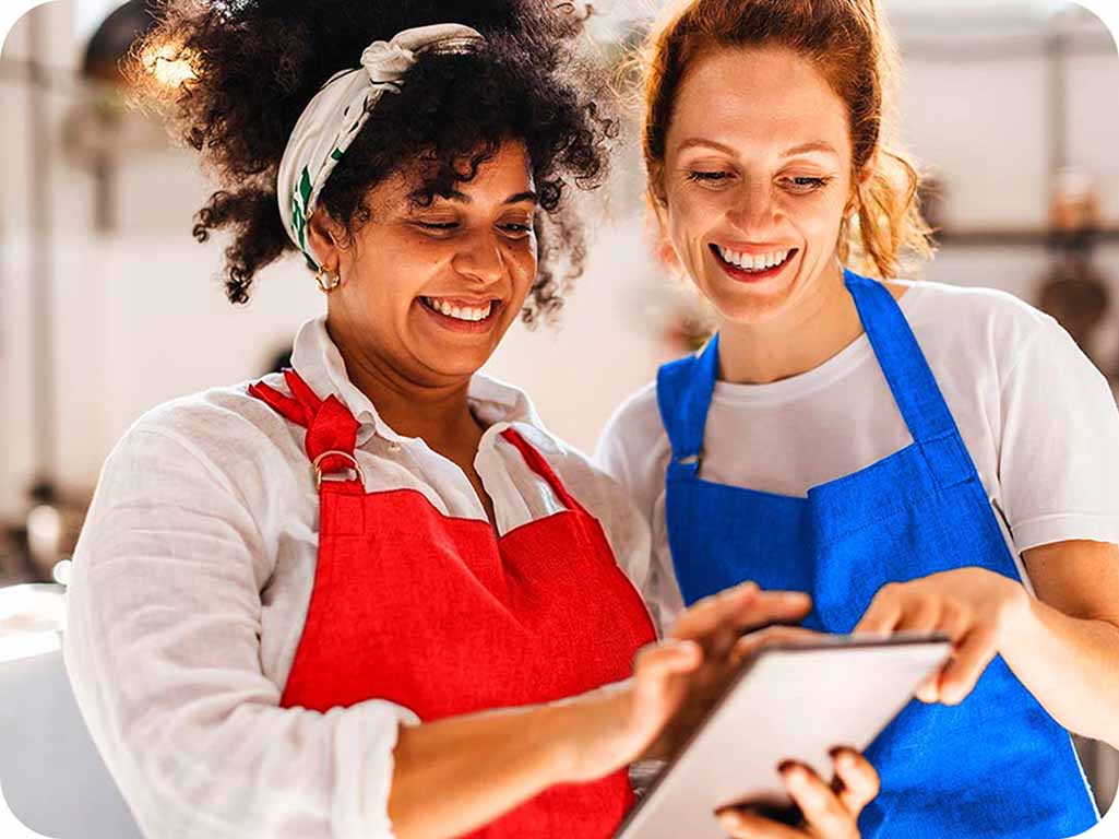 Dos mujeres sonriendo mientras revisan contenido en la tablet