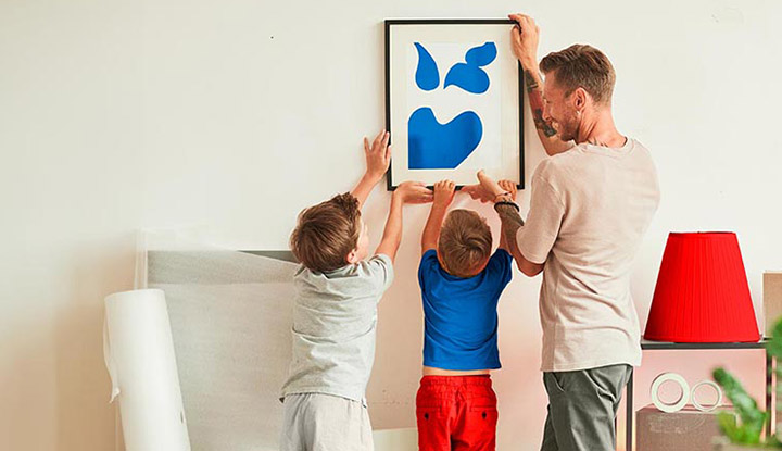 Padre con sus hijos colocando un cuadro en su salón de casa Padre con sus hijos colocando un cuadro en su salón de casa