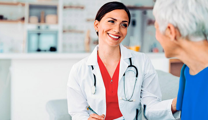 Médico sonriente con bata blanca atendiendo a una persona mayor, simbolizando la atención especializada del seguro Caser Salud +60