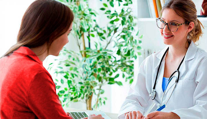 Médico sonriente con bata blanca atendiendo a una paciente que tiene el seguro Caser Salud Prestigio Médico sonriente con bata blanca atendiendo a una paciente que tiene el seguro Caser Salud Prestigio