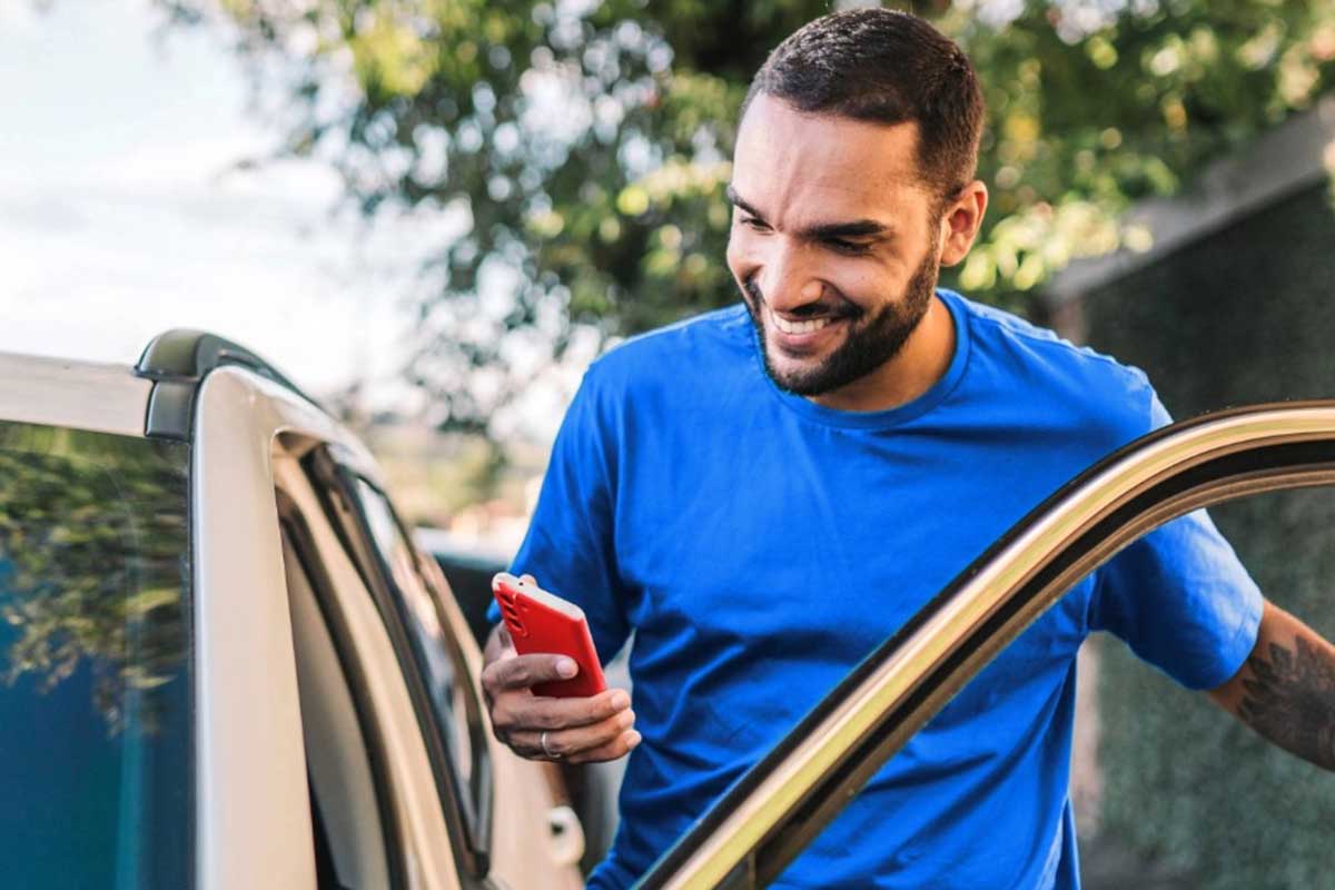 Hombre sonriente entrando en su coche mientras revisa su teléfono móvil
