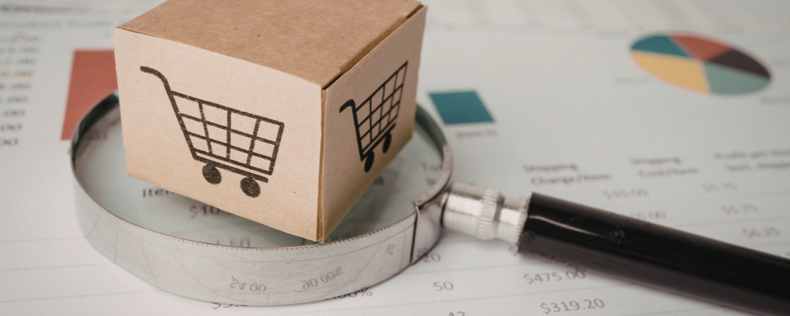 Caja de cartón con el dibujo de un carro de compra sobre una lupa y un informe financiero