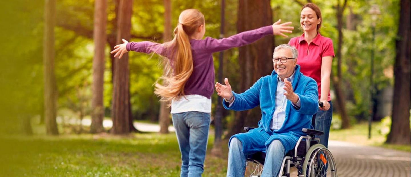 Imagen persona mayor en silla de ruedas abriendo los brazos a una niña en el parque