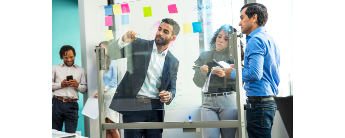 Equipo de profesionales colaborando frente a un panel de cristal con notas adhesivas