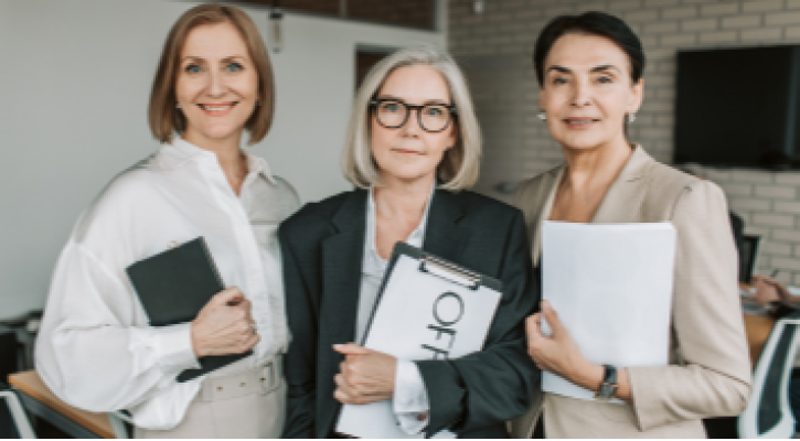 Tres mujeres con documentos en las manos, sonriendo a cámara