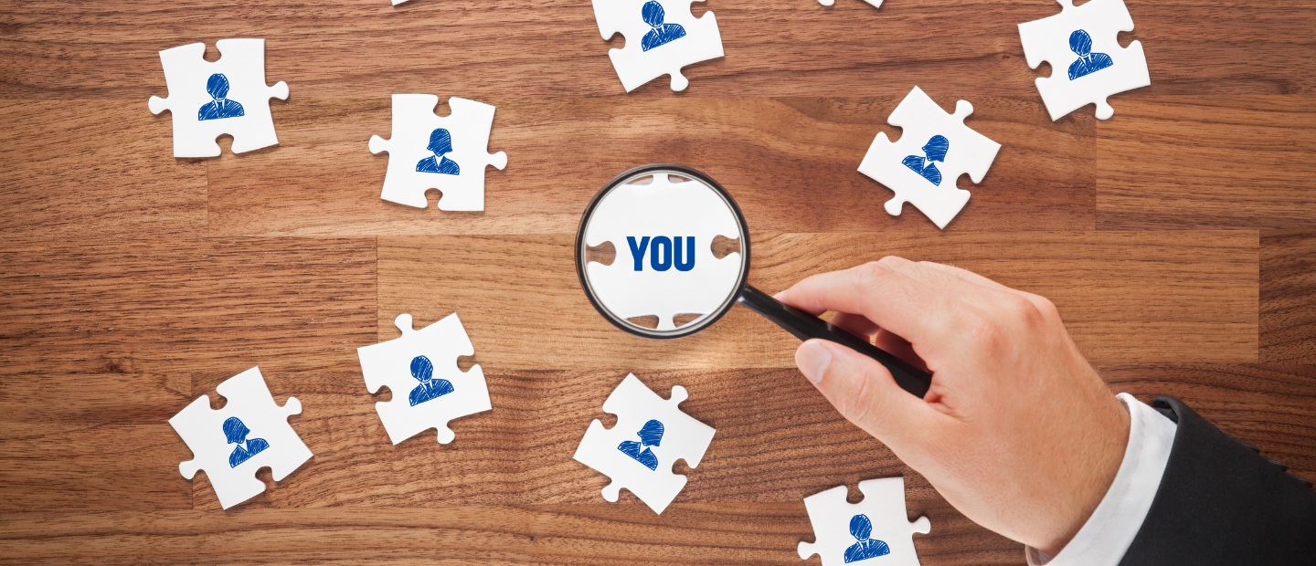 Piezas de puzzle con la representación de personas y una mano con una lupa destacando la pieza central en la que pone You