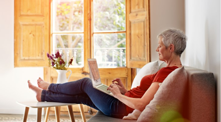 Mujer consulta información en su ordenador en el sofá con el sol entrando por la ventana