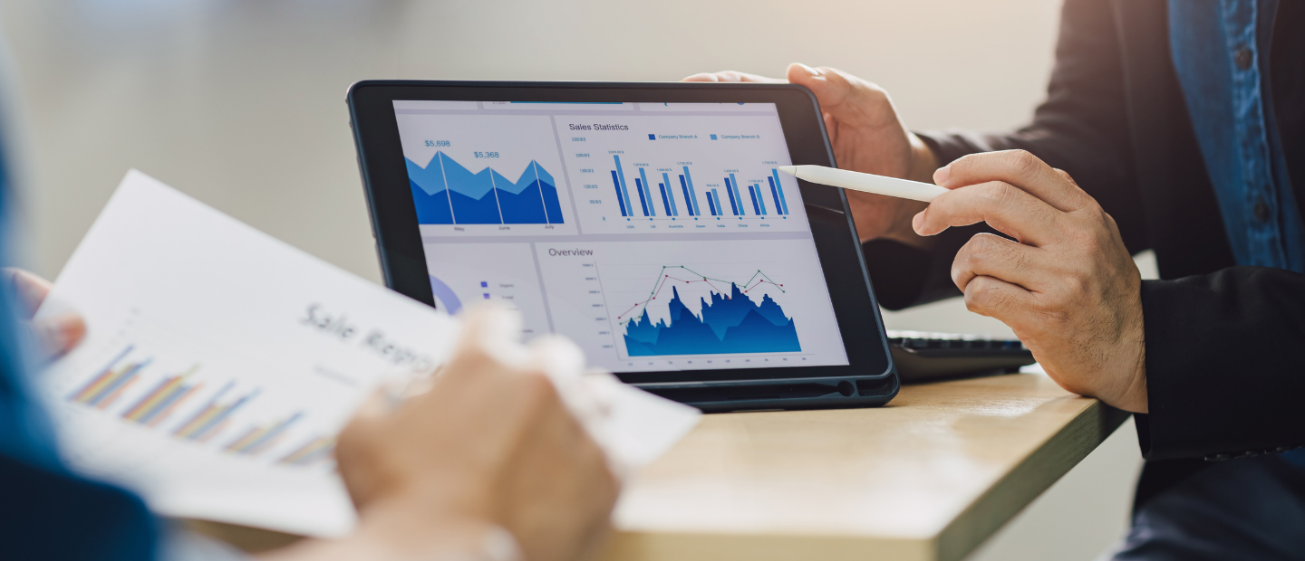 Dos personas analizando gráficos en una tablet y en documentos impresos.